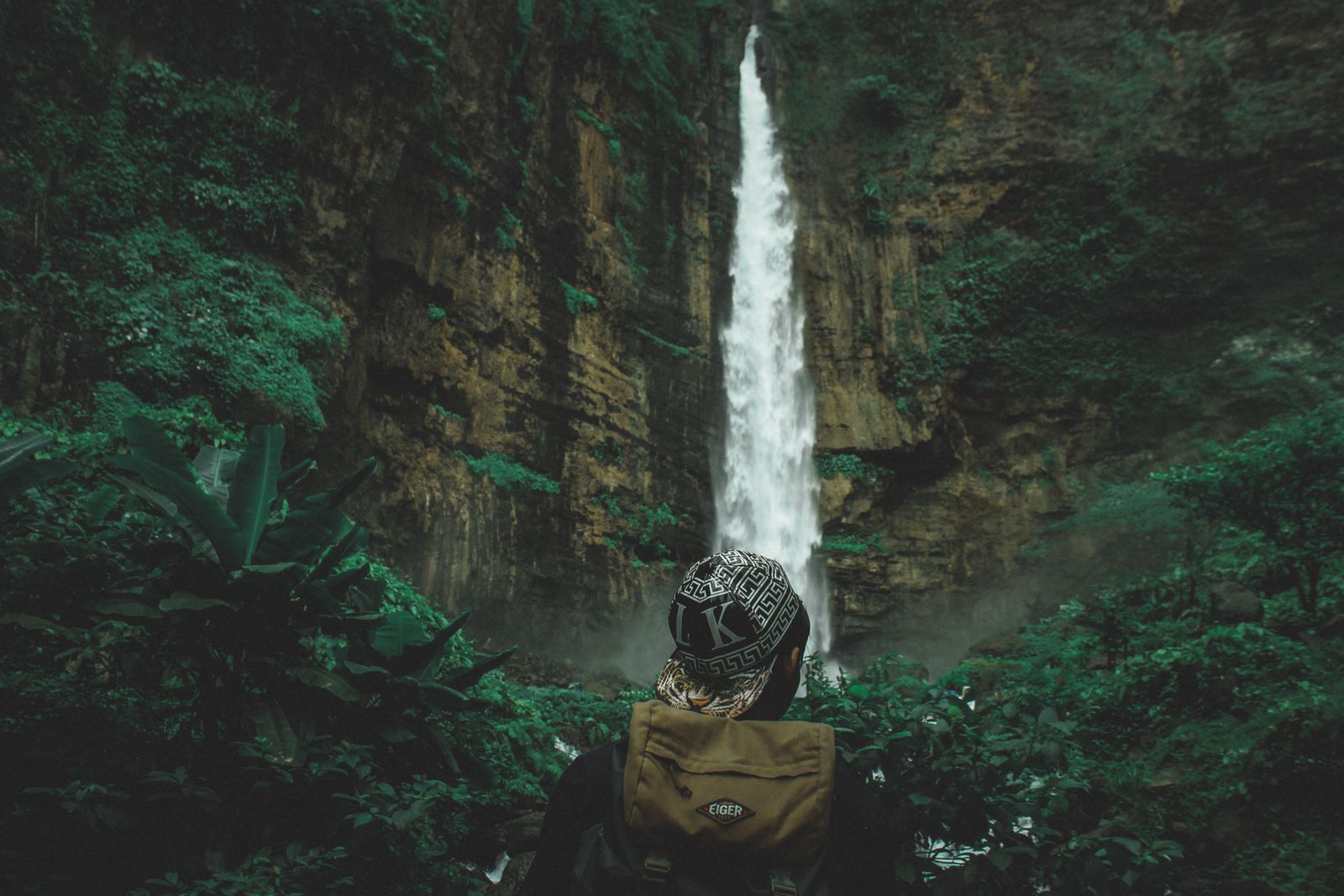 Traveller on the rocks looking up at a tall jungle waterfall, deciding if Sekumpul Waterfall is worth it